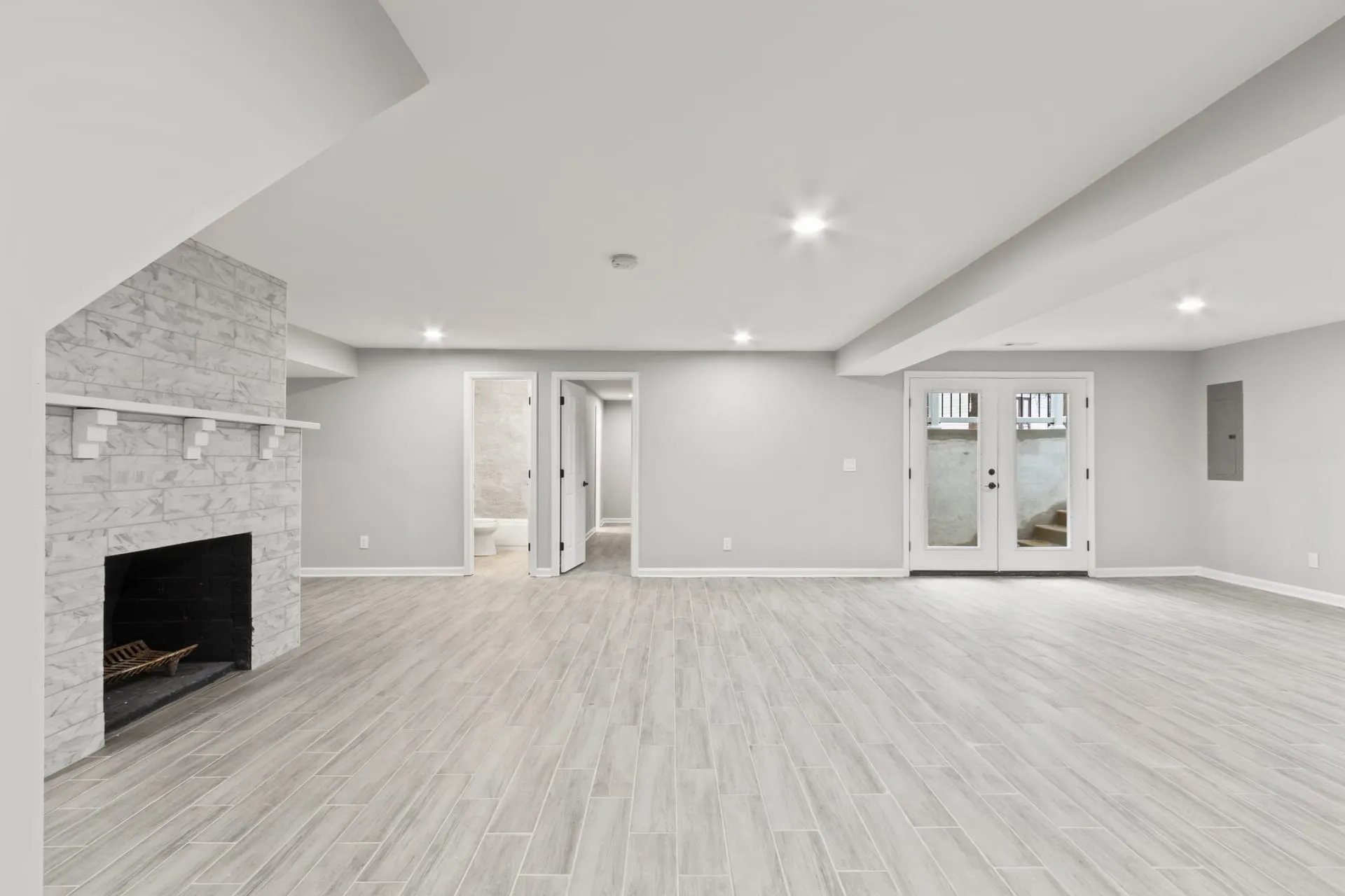 Open finished basement with a tile fireplace and walkout doors by Timeless Builder Group